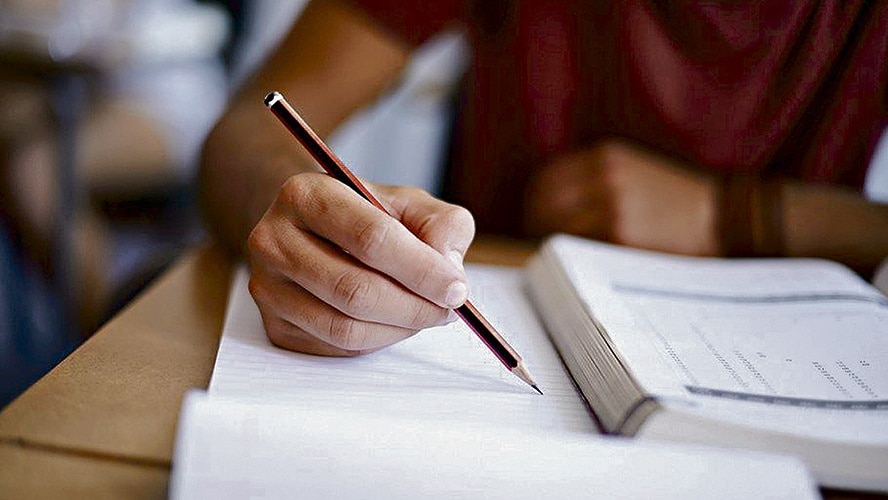 foto de uma pessoa escrevendo, onde aparece um livro, um caderno e um lápis.